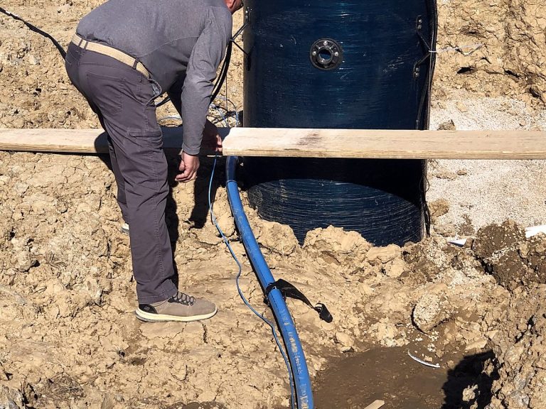 Plumber working in an open trench beside a blue drum