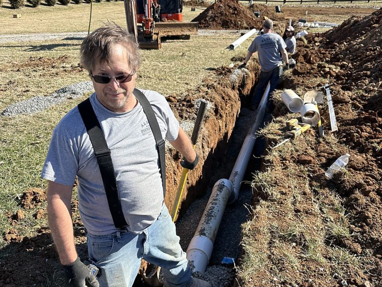 Plumber standing in a trench with an excavator behind