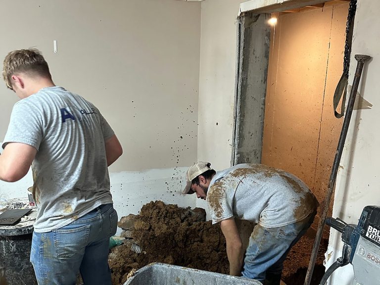 Two plumbers digging inside a building for a drain repair