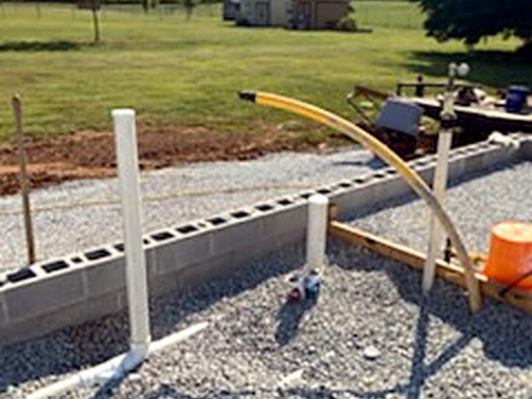 Plumbing stub-outs in a gravel slab pad with a house behind