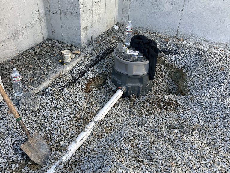 Sump basin in gravel beside a poured foundation wall