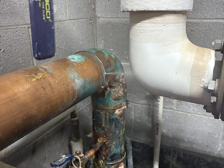 Corroded copper pipe fitting on a block wall