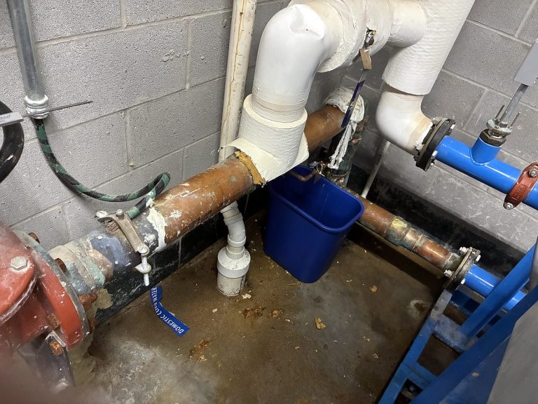 Copper and PVC pipe repair in progress with a bucket beneath