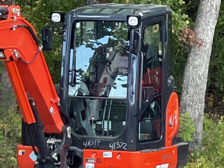 Orange mini excavator beside a tree