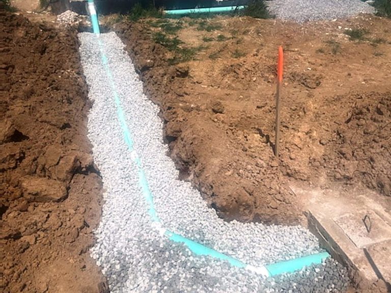 Sewer line in a gravel-bedded trench beside a house