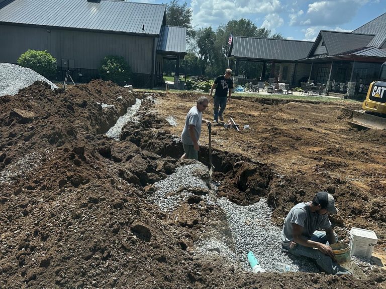 Two plumbers laying pipe in a wide excavation