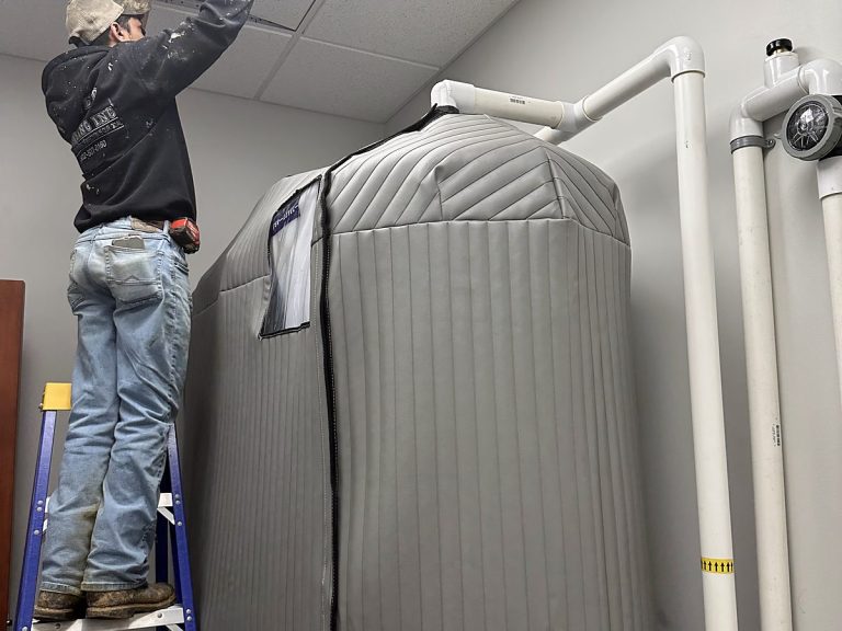 Plumber on a ladder beside a large insulated water heater