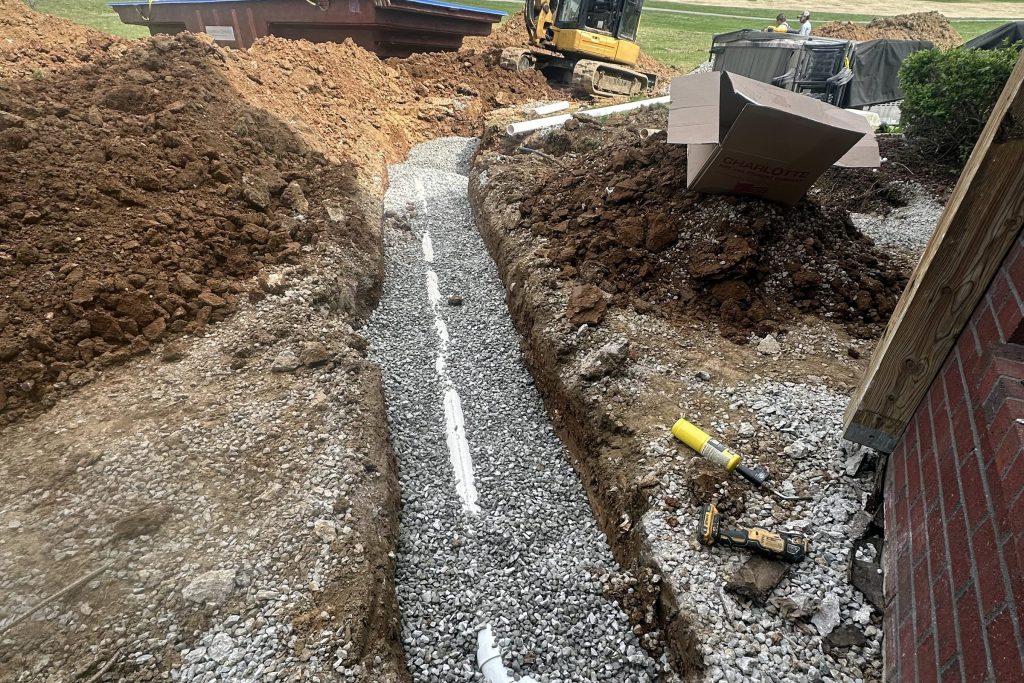Sewer line in a trench across a yard, excavator at the far end