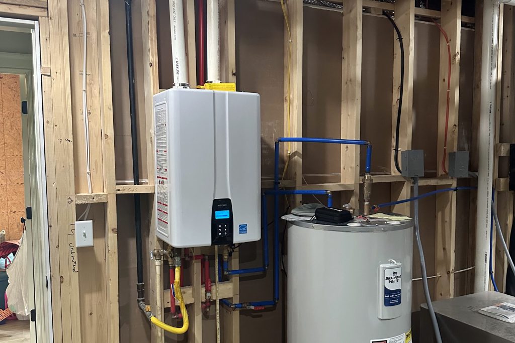 Tankless and tank water heaters in a framed utility room on a new build